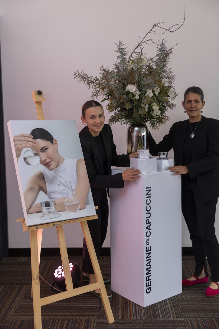Anfitrionas de traje negro junto a pedestal de marca, arreglo floral y caballete de campaña