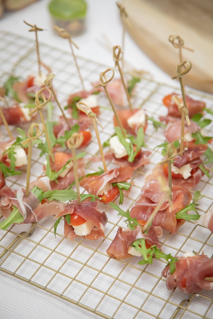 Brochetas de prosciutto, rúgula, tomate y queso sobre rejilla dorada