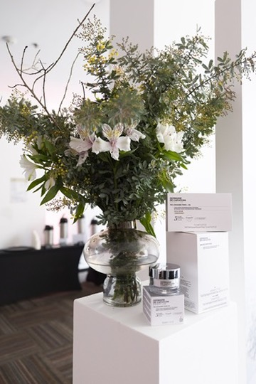 Arreglo floral botánico sobre pedestal blanco junto a la línea de producto
